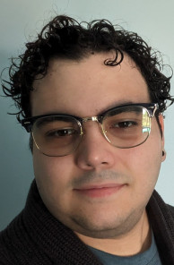 Young man with dark curly hair wearing gold rim glasses